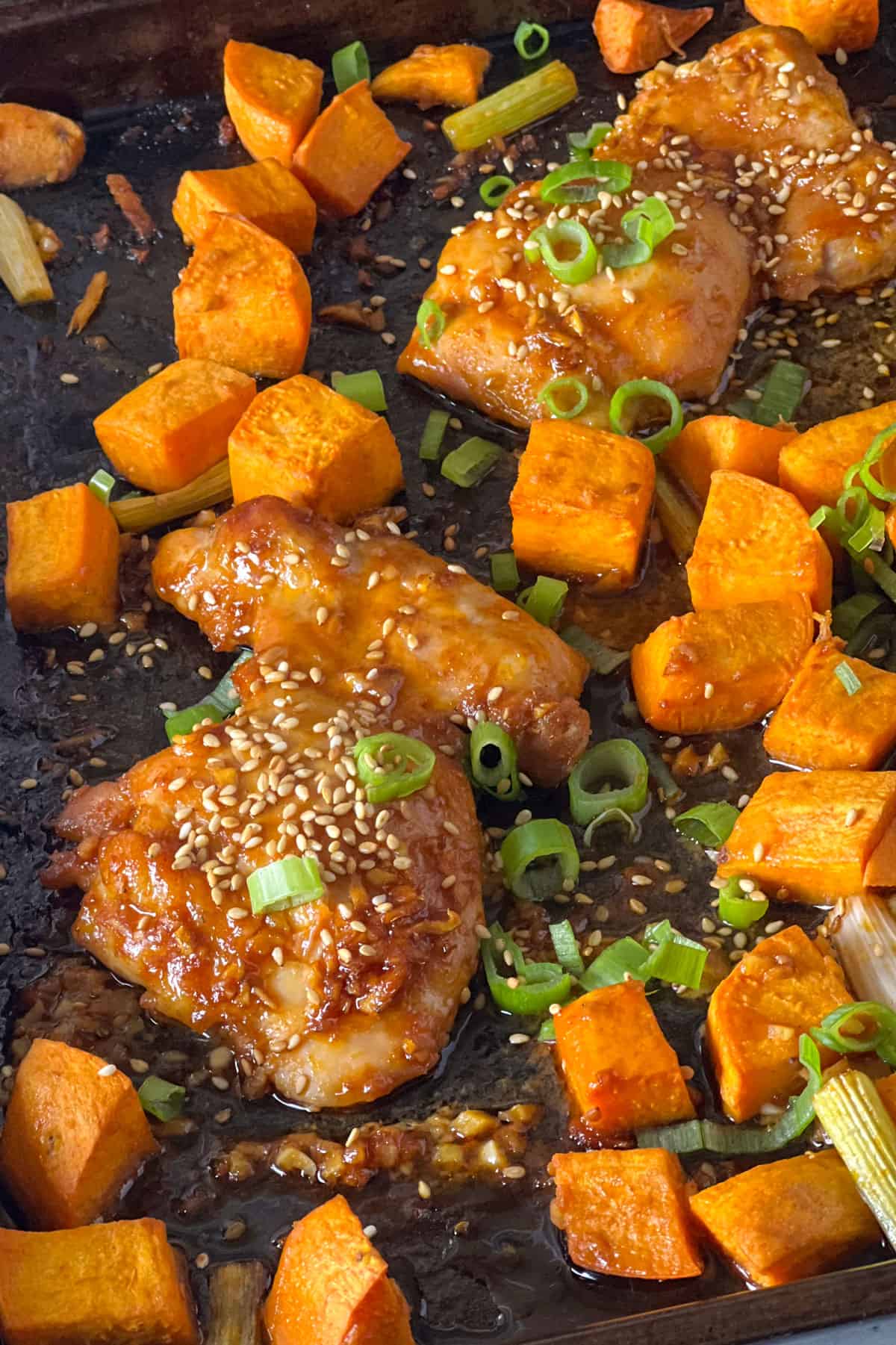Sheet pan with fried potato cubes, boneless chicken thigh with gochujang sauce, sesame seeds and chopped scallions.