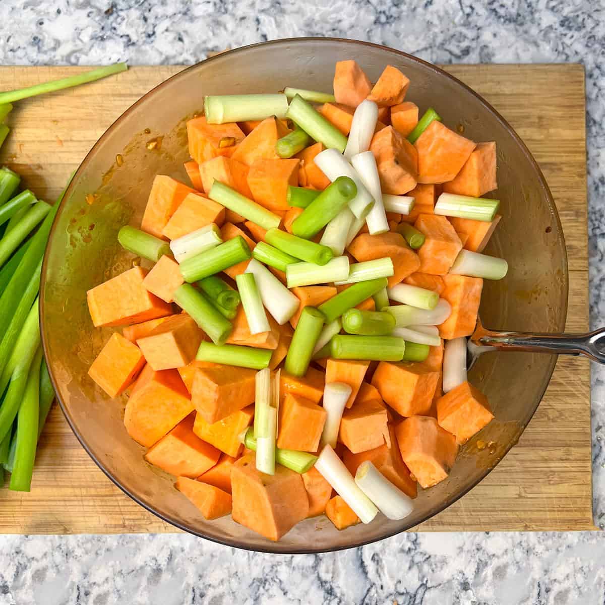 Cubes of raw potatoes and 1-inch pieces of bread are tossed together in a glass mixing bowl.