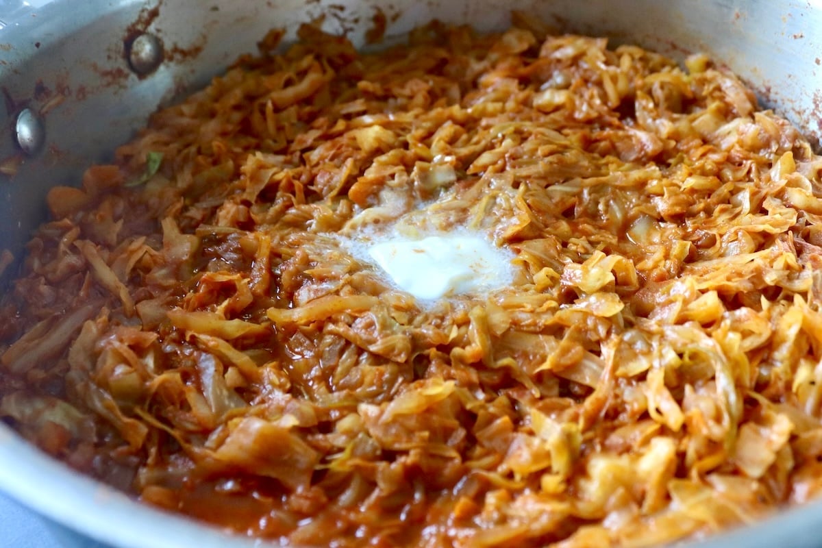 Cooked and wilted cabbage with tomato sauce in a pan with melted butter on top.
