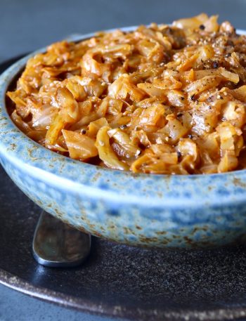 Light blue ceramic bowl full of tomato sautéed cabbage, on a dark brown ceramic plate.