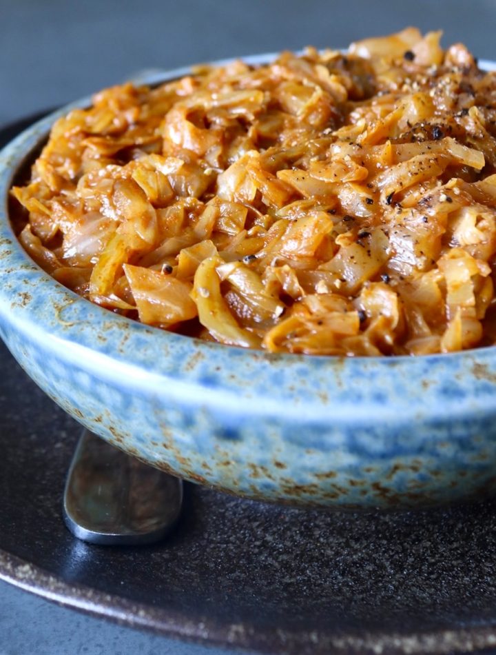 Light blue ceramic bowl full of tomato sautéed cabbage, on a dark brown ceramic plate.