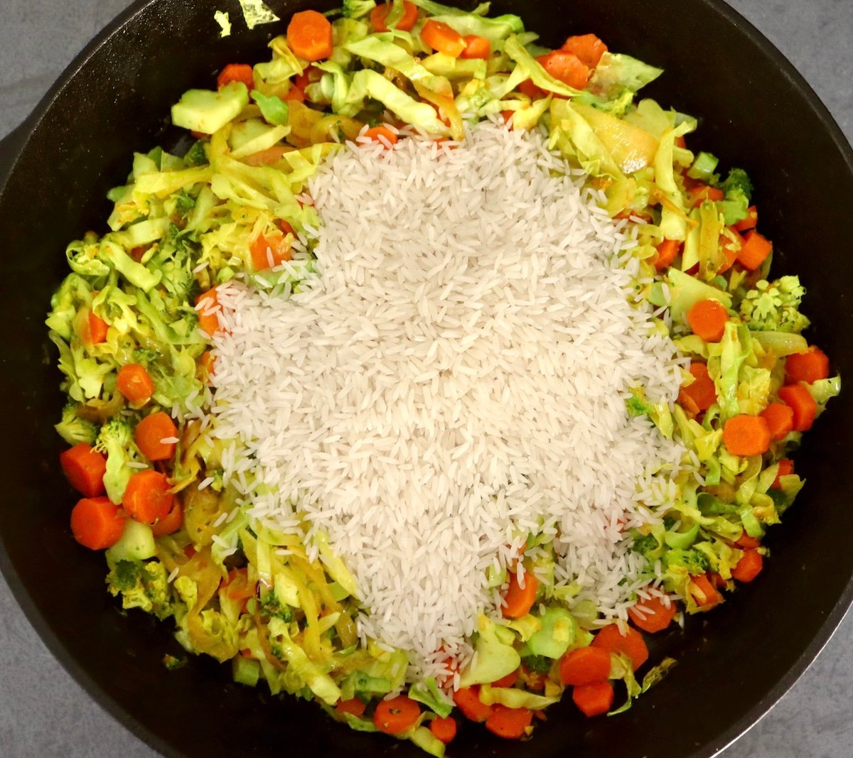Hombe yakakandwa simbi skillet yakazadzwa nesauteed kabichi, broccoli, hanyanisi uye makarotsi, uye murwi wemupunga pamusoro.