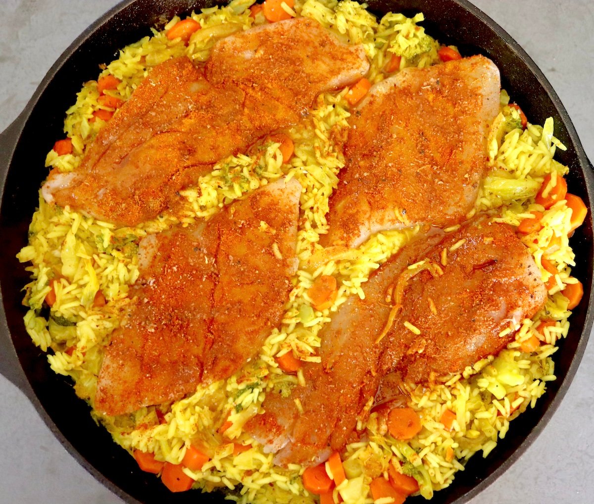 Kanda iron skillet yakazadzwa neyero yemuriwo mupunga uye 4 mbishi, yakavharwa nehove fillet pamusoro.