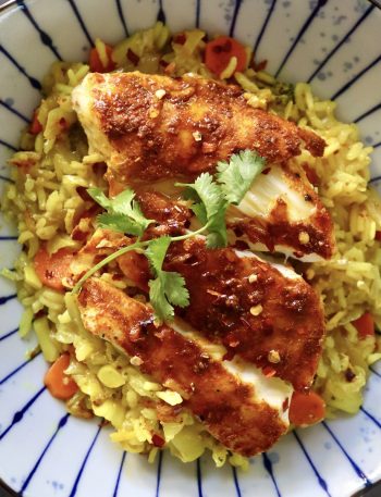 Top View of blue striped plate with yellow rice and sliced, red-spiced fish, with a sprig of cilantro.