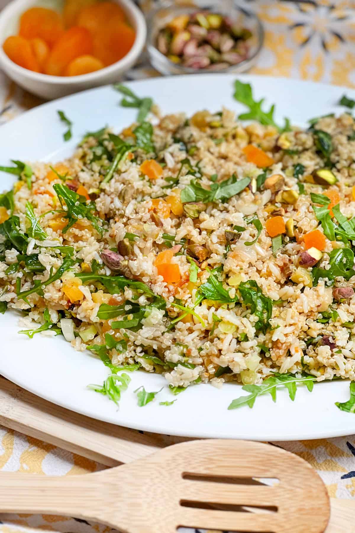 a bowl of rice and quinoa salad with a small bowl of dried apricots and a small bowl of roasted pistachios in the background.