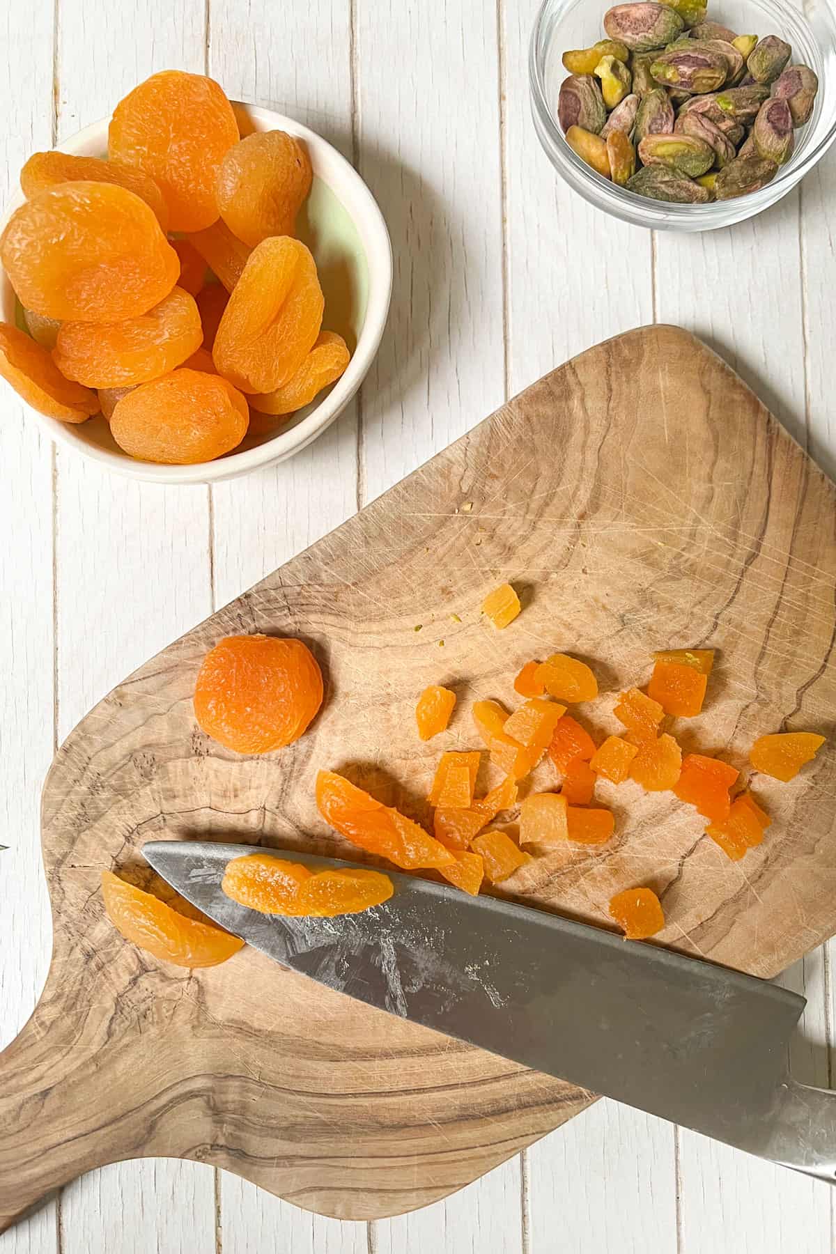 dried apricots in a small bowl and two sliced ​​on a small wooden board next to a small glass bowl of roasted pistachios.