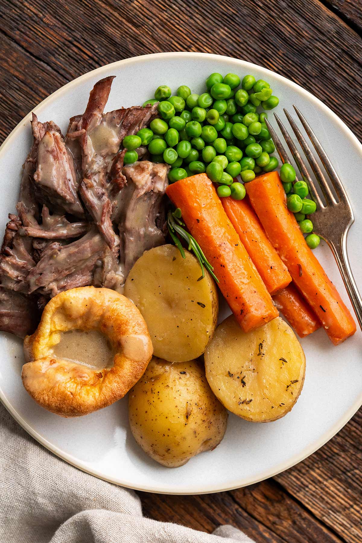 close up of plate of chuck roast pot roast dinner with vegetables and Yorkshire pudding