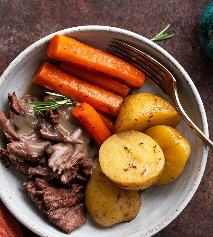 beef chuck roast dutch oven meal plated with vegetables and gravy