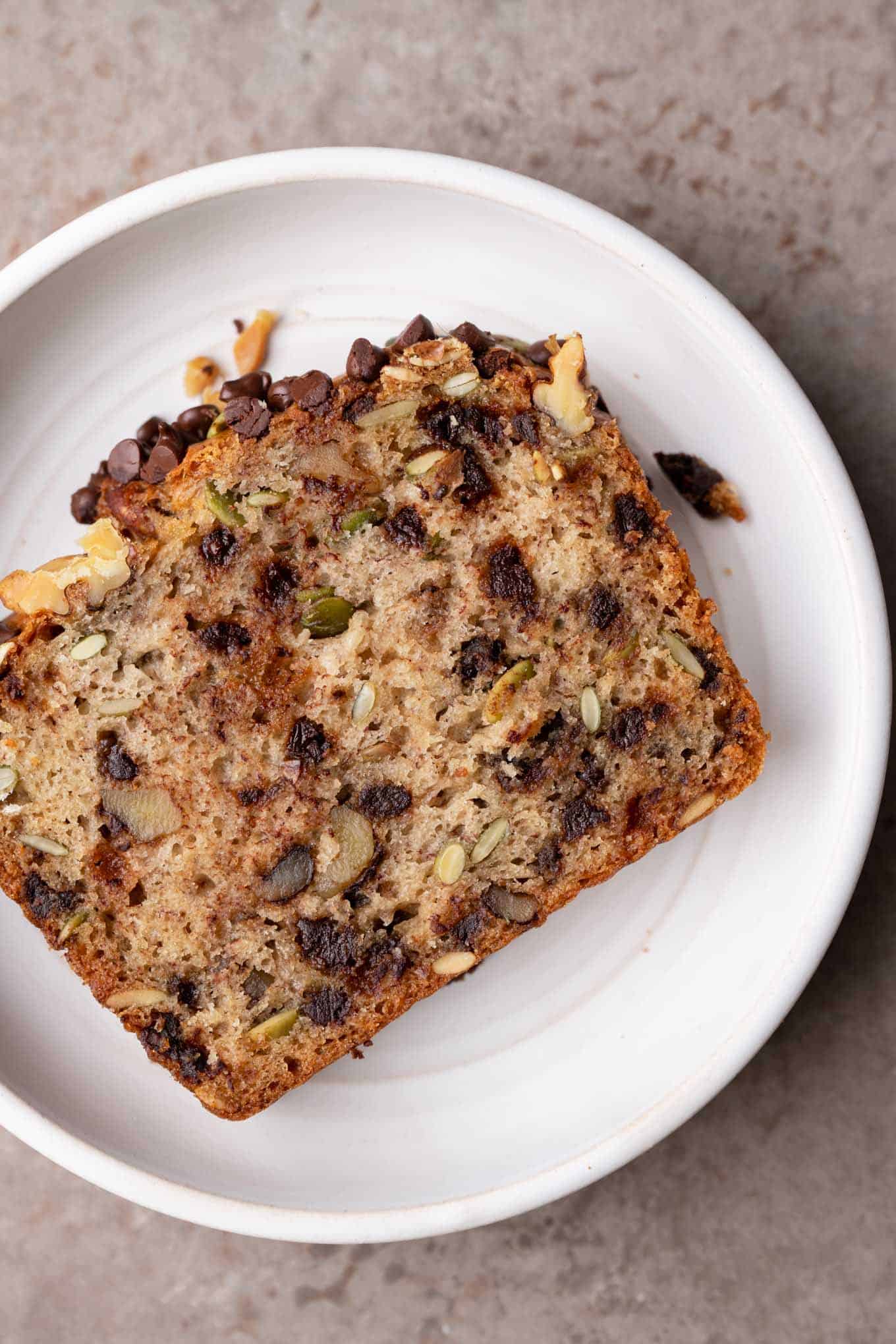 cover shot of a piece of chocolate chip, walnut, pepita banana bread in a plate