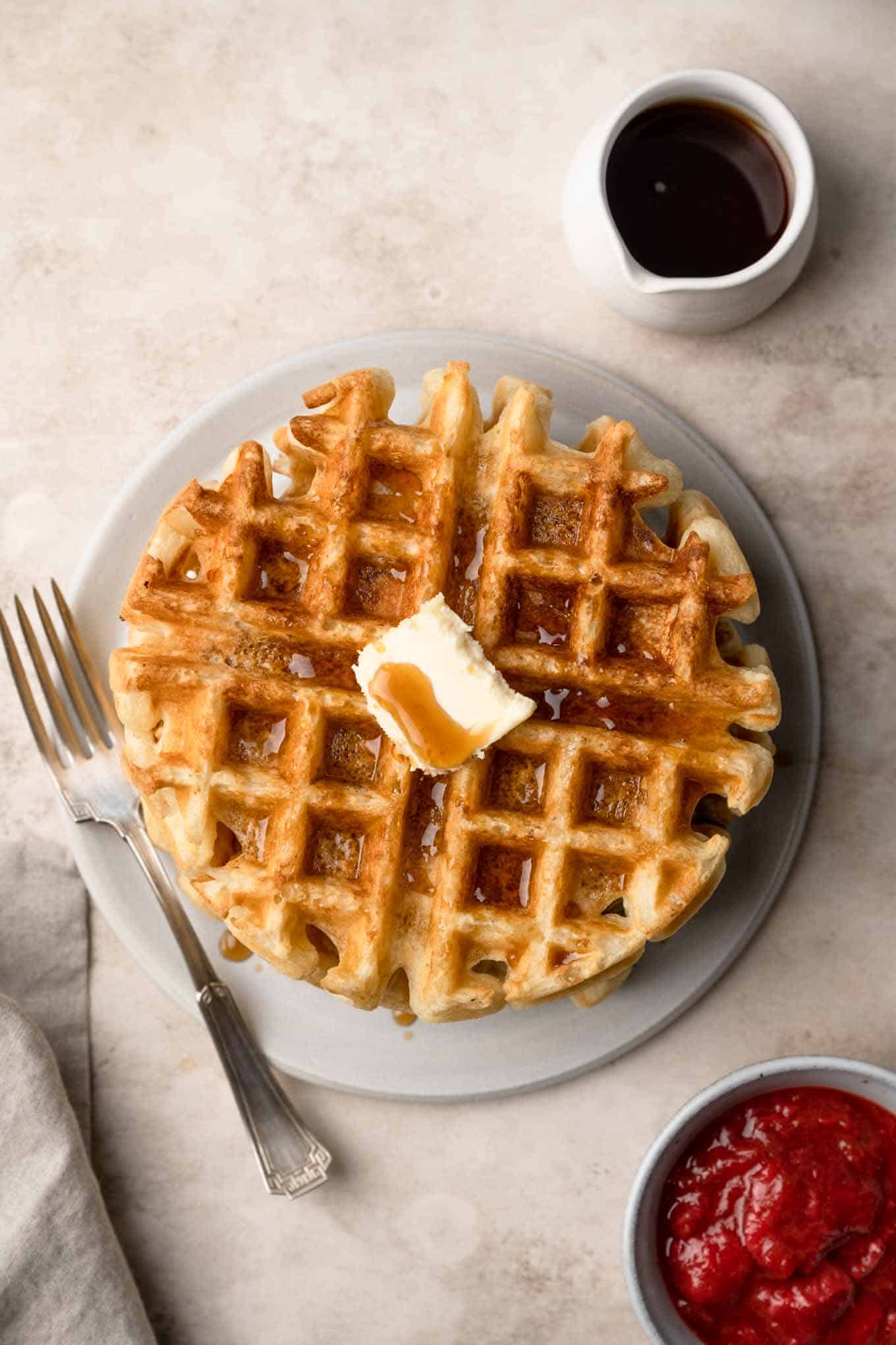 Top shot of a vegan waffle on a plate with maple syrup and a side of berry compote