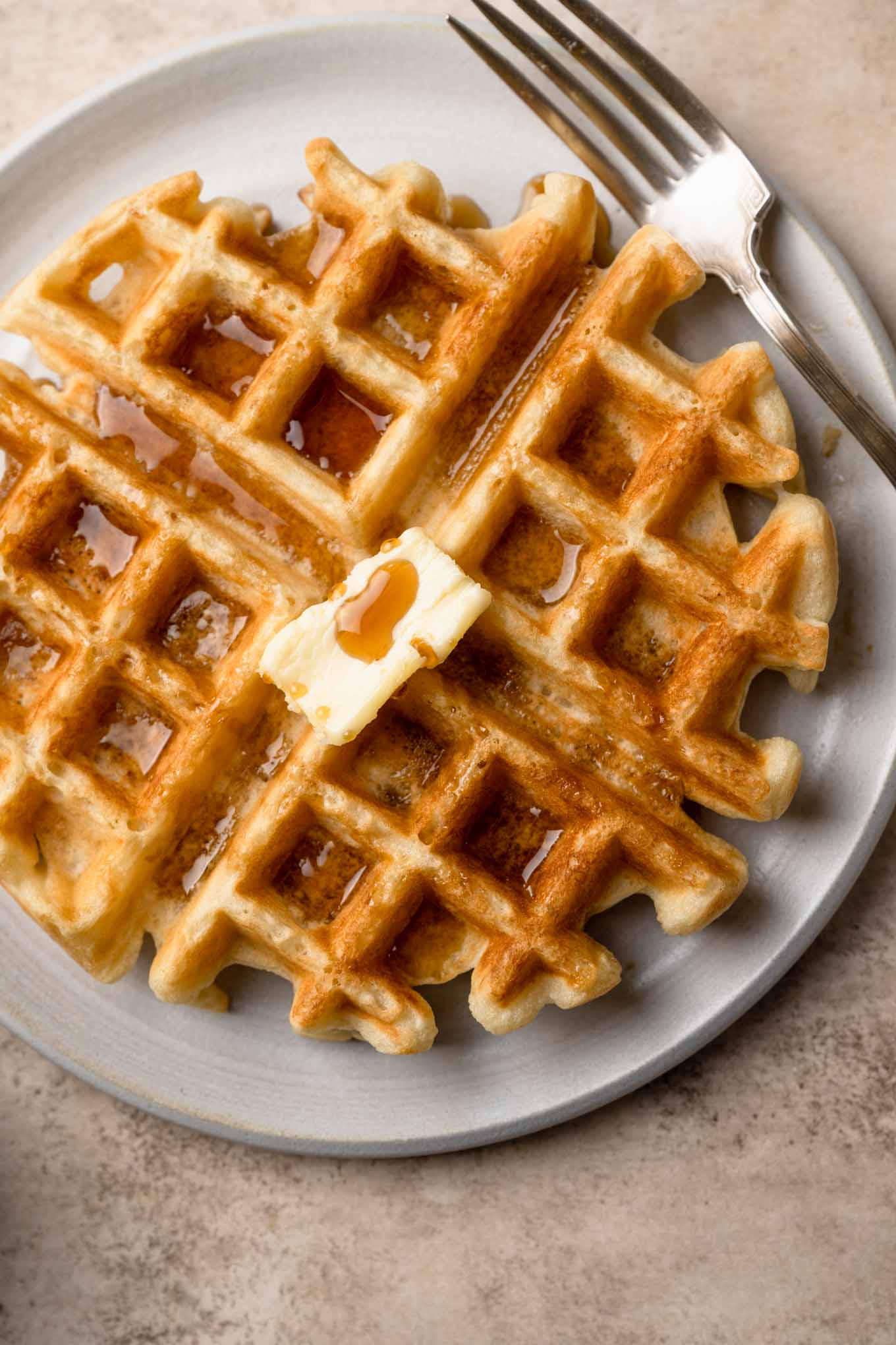 A waffle in a bowl with maple syrup combined in a bag and topped with vegan butter