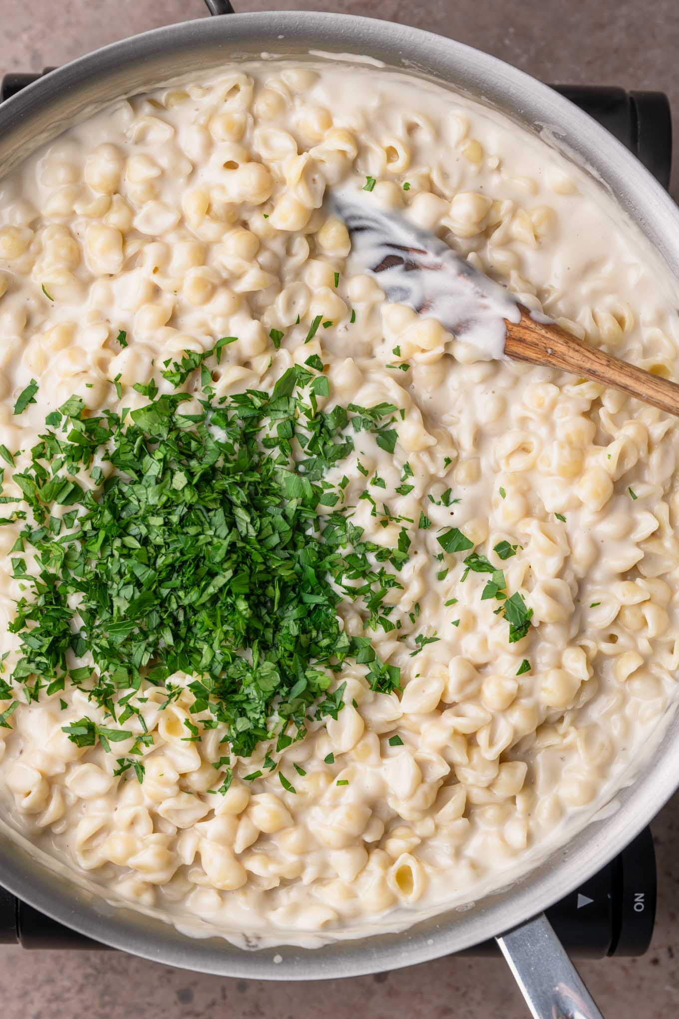 mini shells, creamy garlic sauce, and chopped parsley in a pot are stirred together