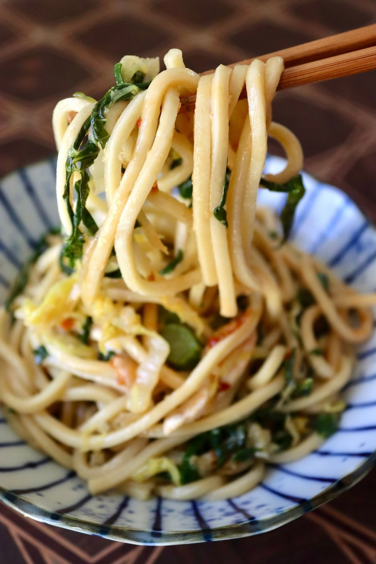 Serving Chinese Longevity Noodles with Gai Lan on a ceramic blue and white plate with a bite raised on chopsticks.