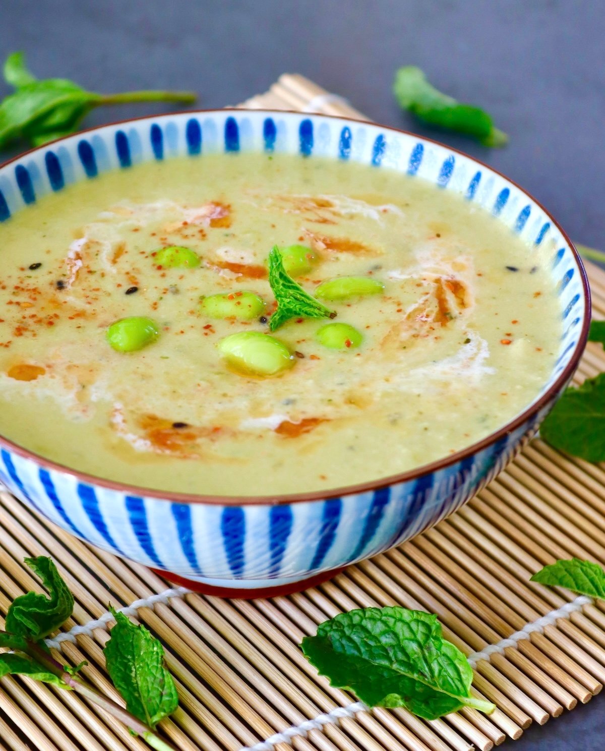 Blue and white striped, ceramic bowl with edamame soup with chili oil, mint leaf, and cream.