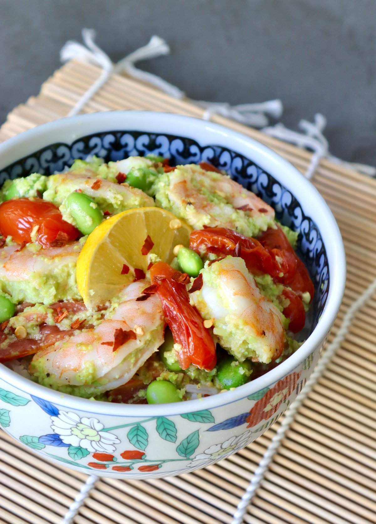 Ceramic bowl with colorful flowers, filled with shrimp, tomatoes and edamame over rice.